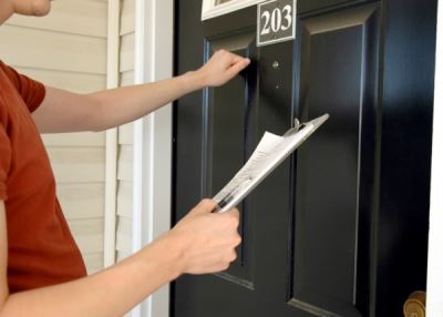 Someone knocking on a door holding a paper